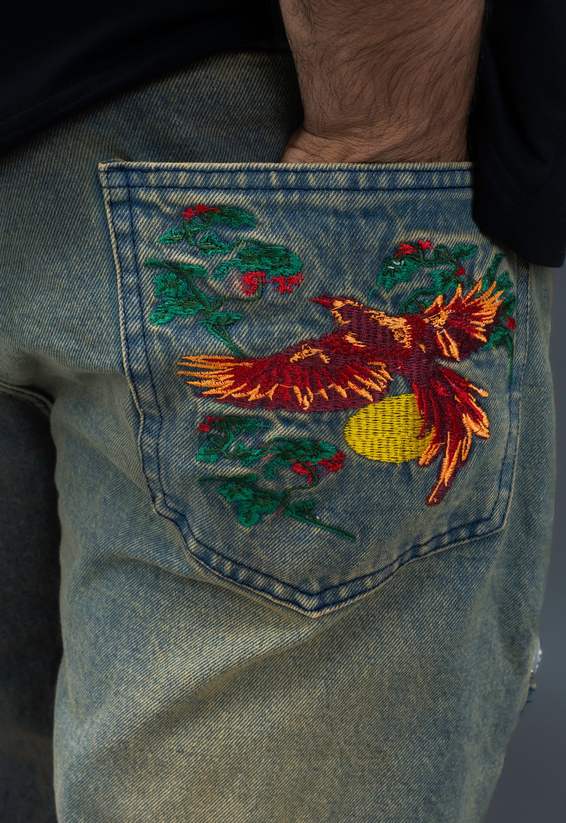Embroidered design on a denim fabric with a bird and floral elements.