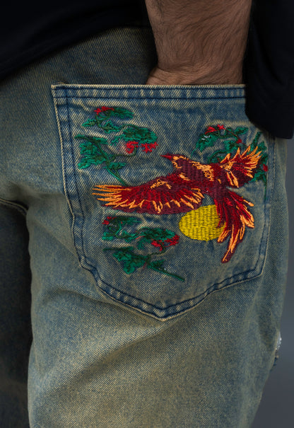 Embroidered design on a denim fabric with a bird and floral elements.
