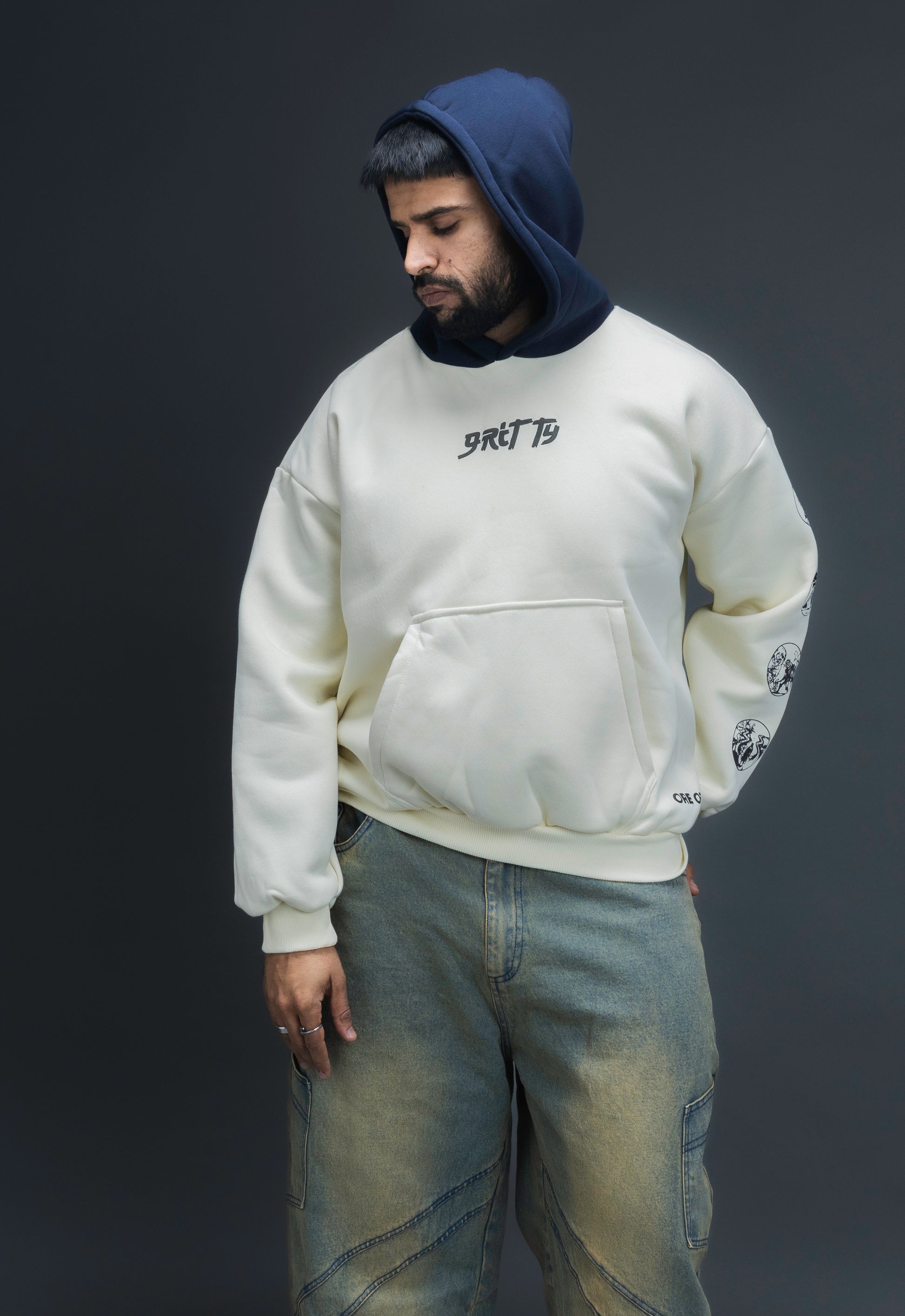 Person wearing a off-white contrast hoodie by ORE OFE with text on the chest that reads GRITTY, standing against a black background