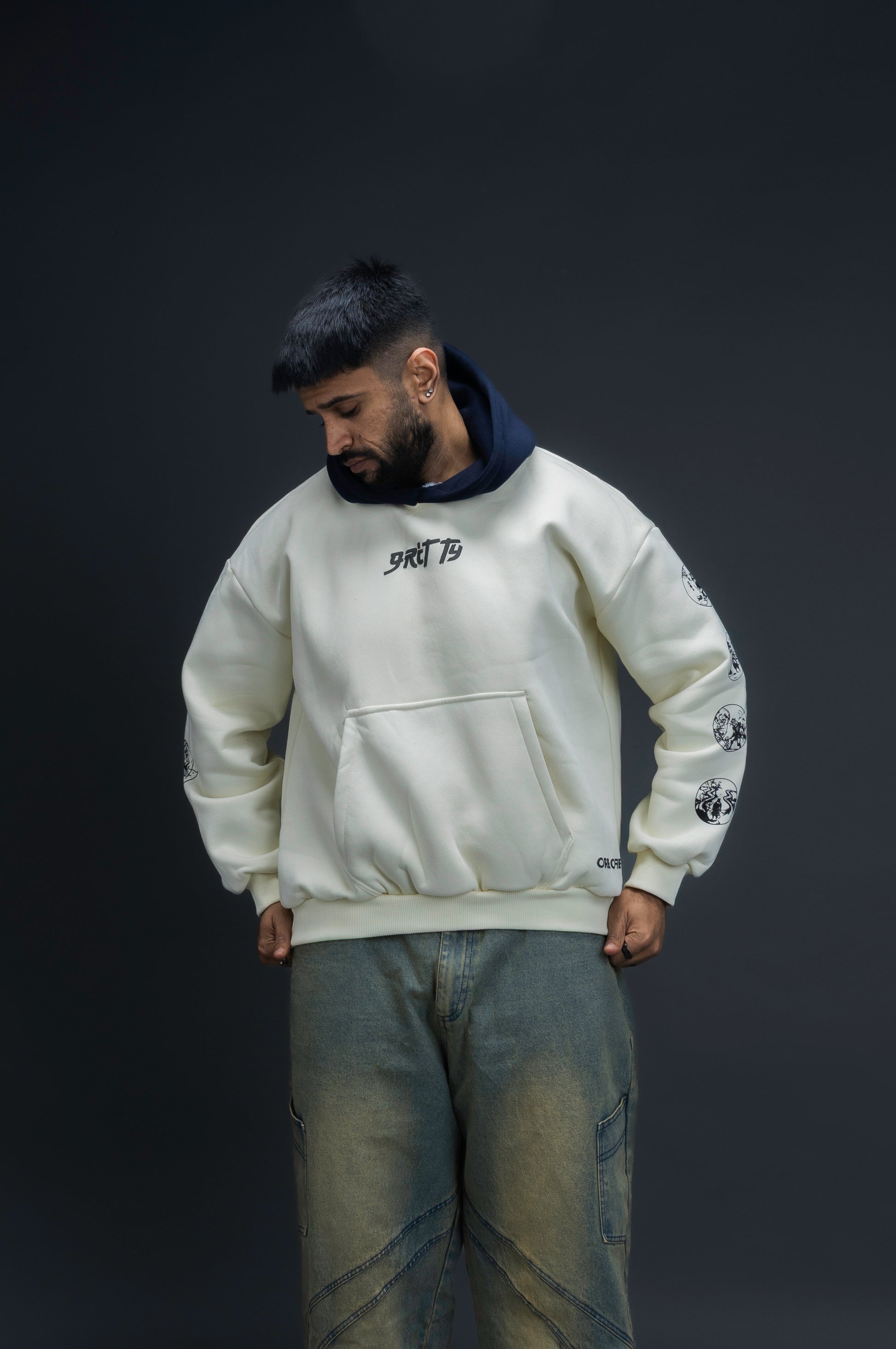 Person wearing a off-white contrast hoodie by ORE OFE with text on the chest that reads GRITTY & design on both sleeves, standing against a black background 