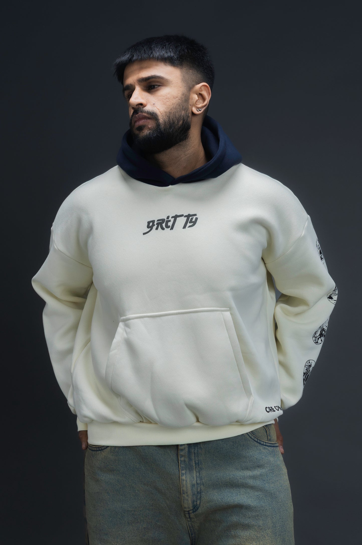 Person wearing a off-white contrast hoodie by ORE OFE with text on the chest that reads GRITTY & design on both sleeves, standing against a black background 