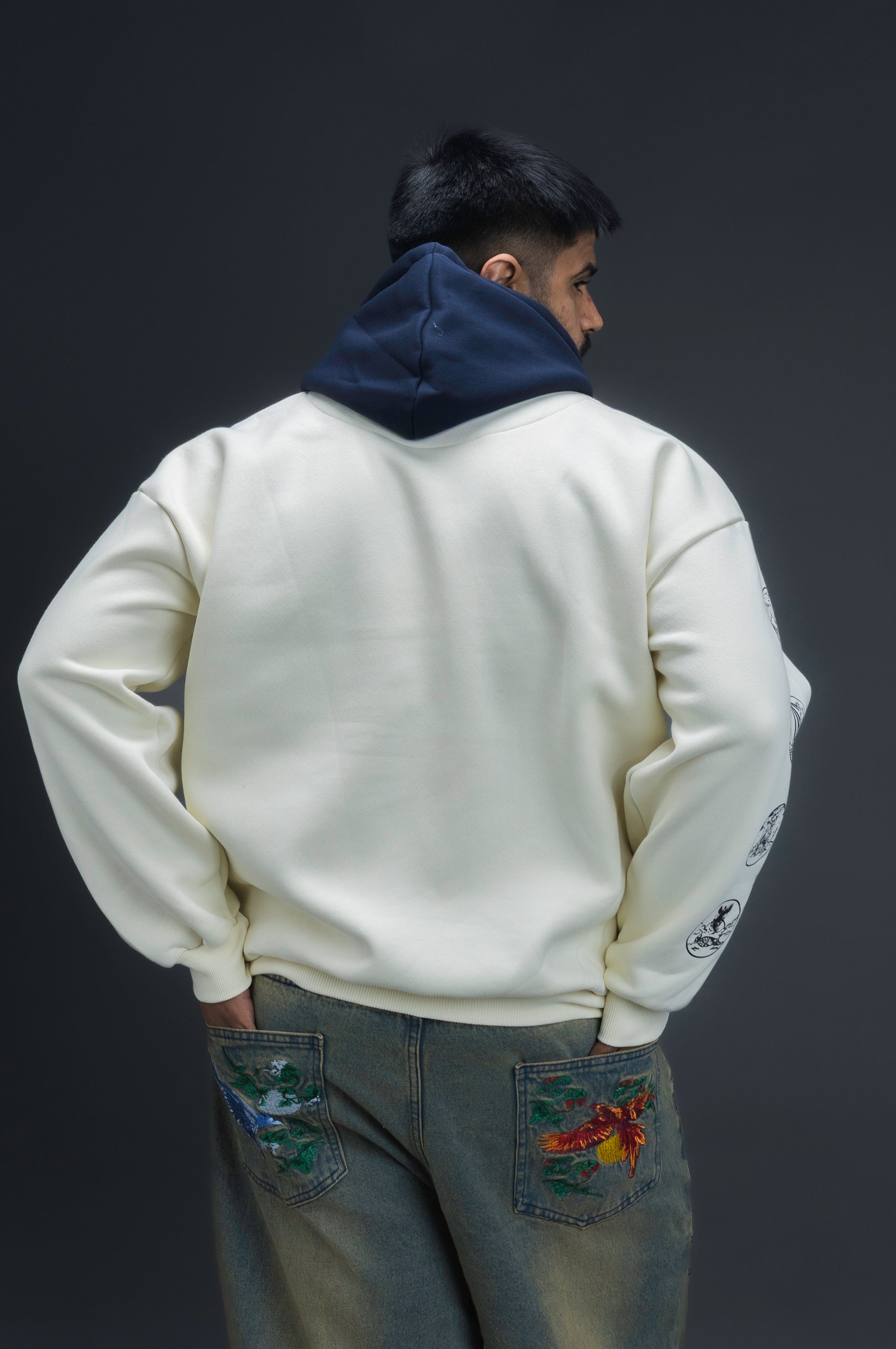 Person wearing a off-white contrast hoodie by ORE OFE with text on the chest that reads GRITTY & design on both sleeves, standing against a black background 