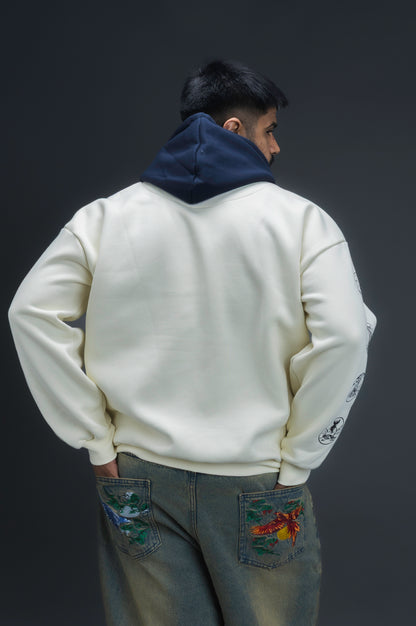 Person wearing a off-white contrast hoodie by ORE OFE with text on the chest that reads GRITTY & design on both sleeves, standing against a black background 