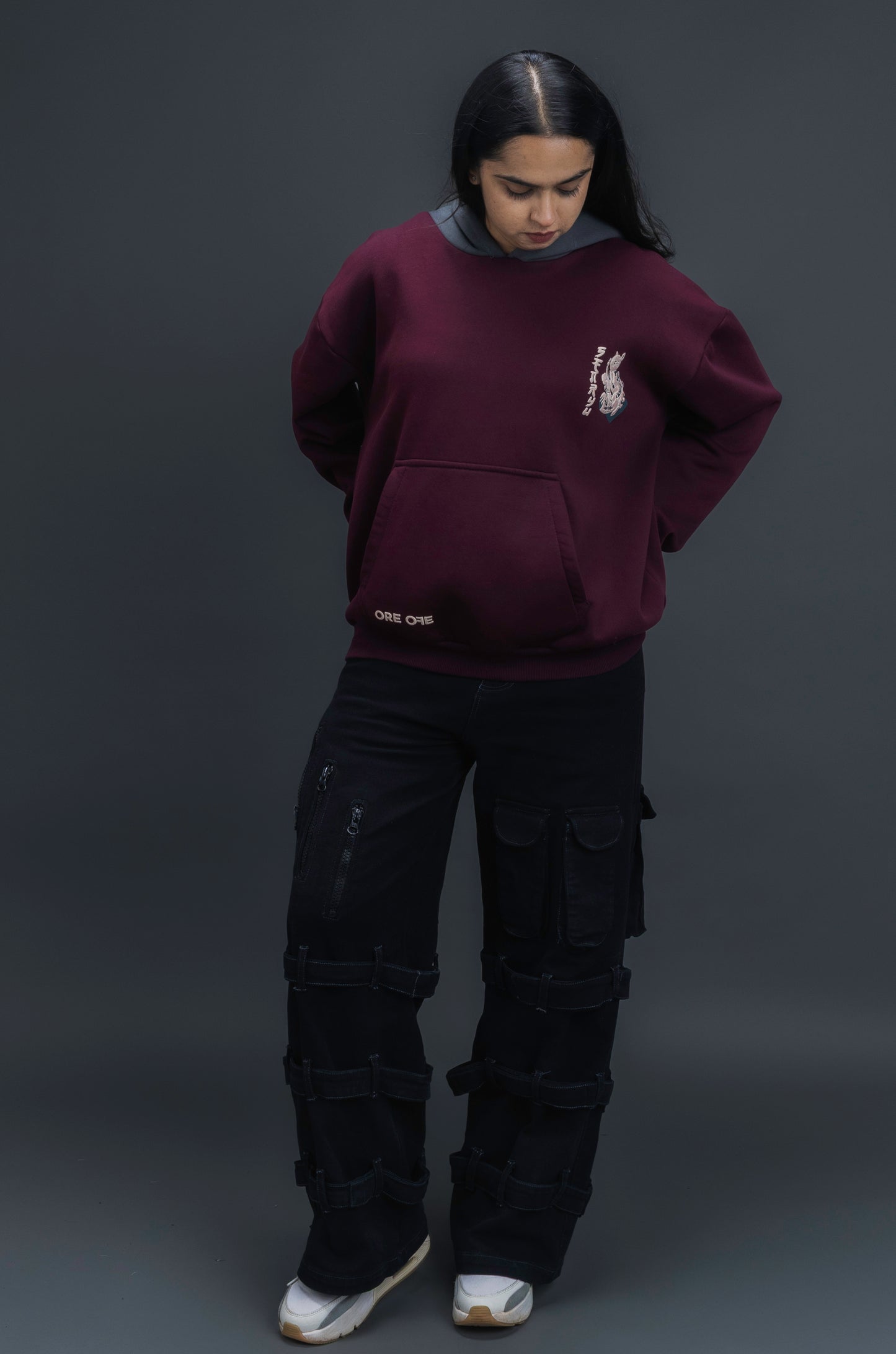 Person wearing a maroon contrast hoodie by ORE OFE with chest & back puff printed design  standaing against  a dark grey background