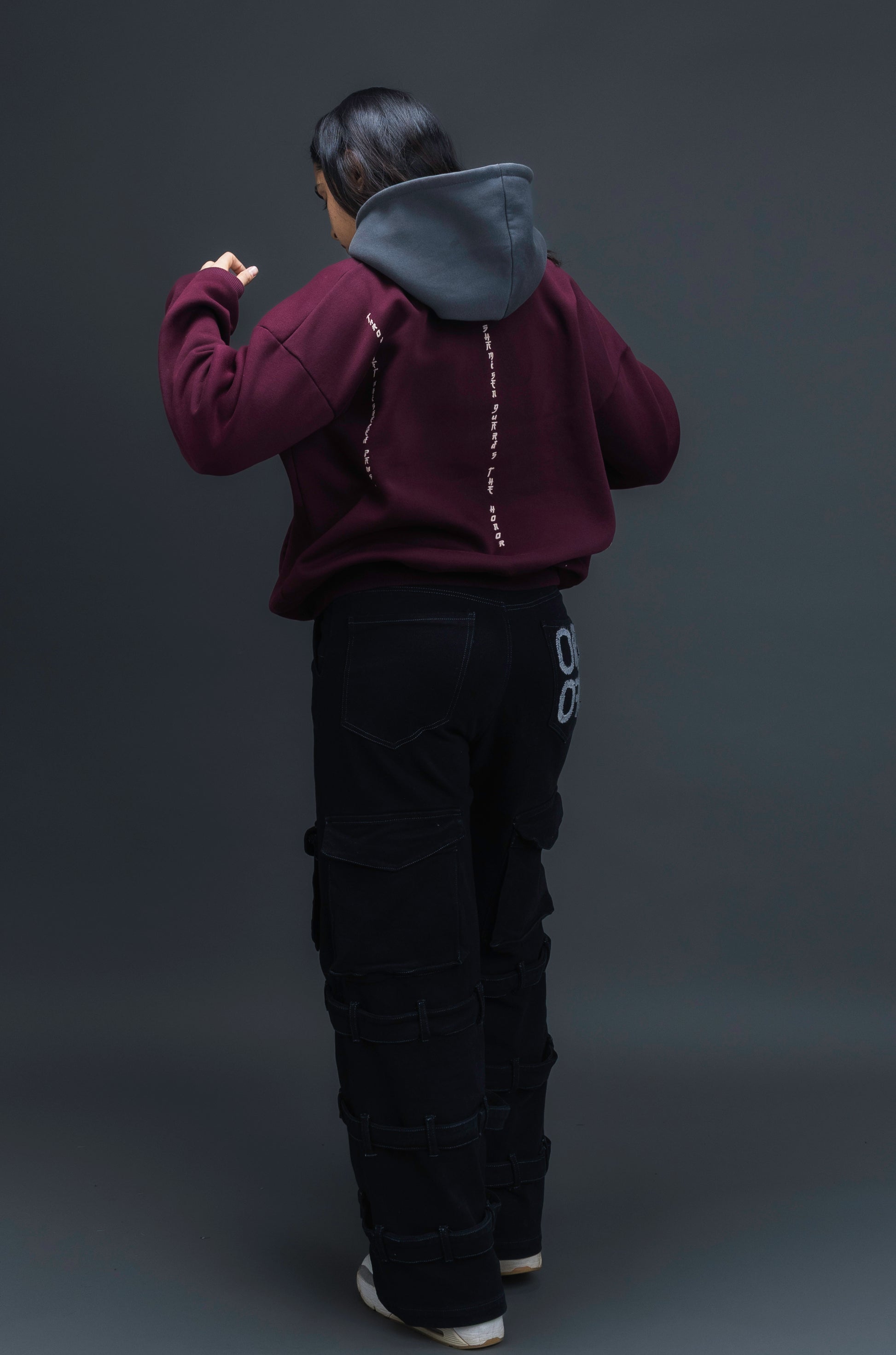 Person wearing a maroon contrast hoodie by ORE OFE with chest & back puff printed design  standaing against  a dark grey background