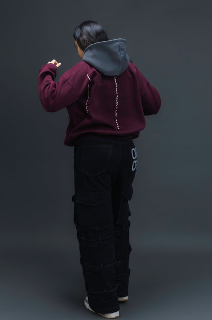 Person wearing a maroon contrast hoodie by ORE OFE with chest & back puff printed design  standaing against  a dark grey background