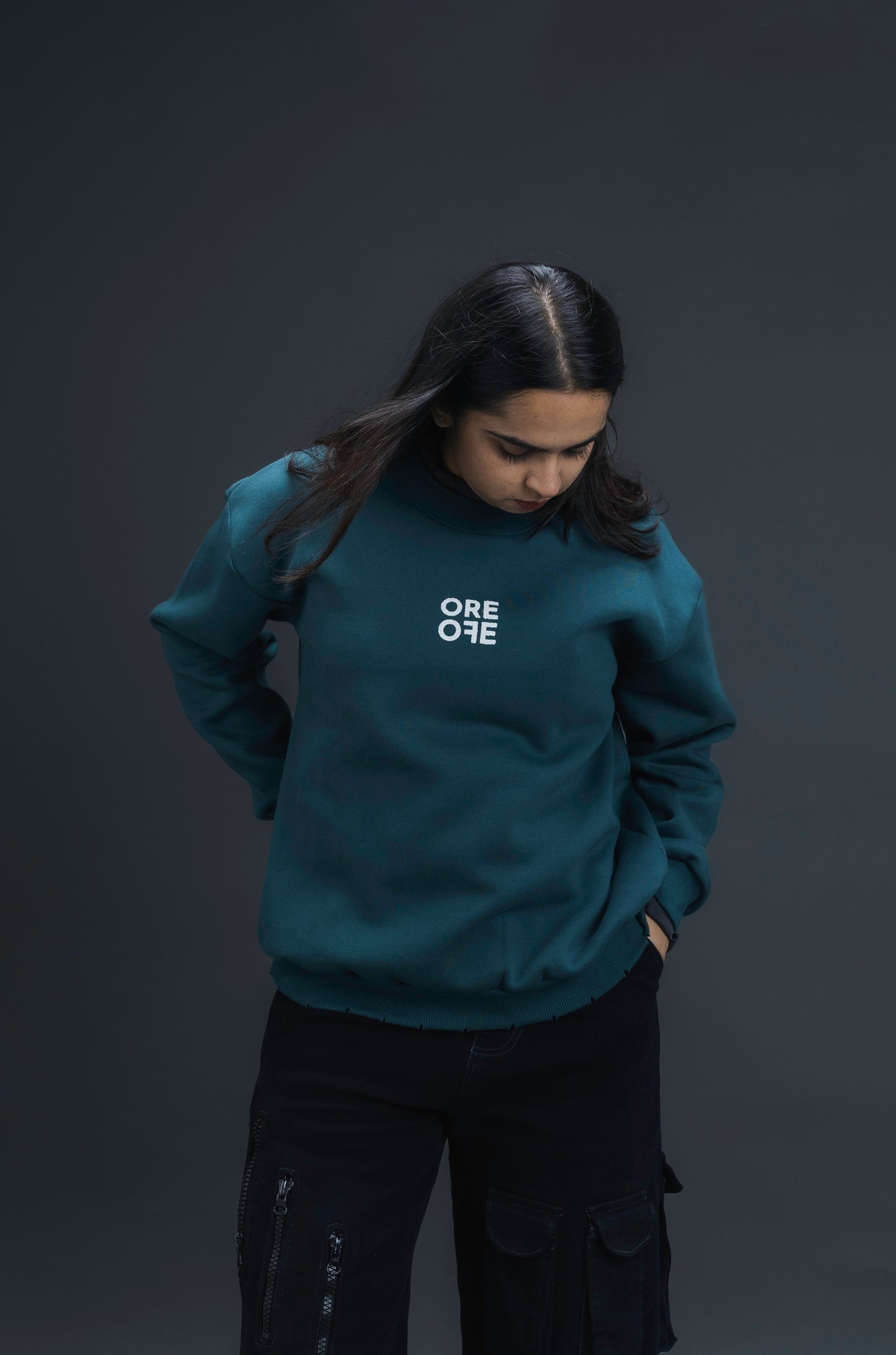 Person wearing a teal sweater with ORE OFE logo on the centre of the chest