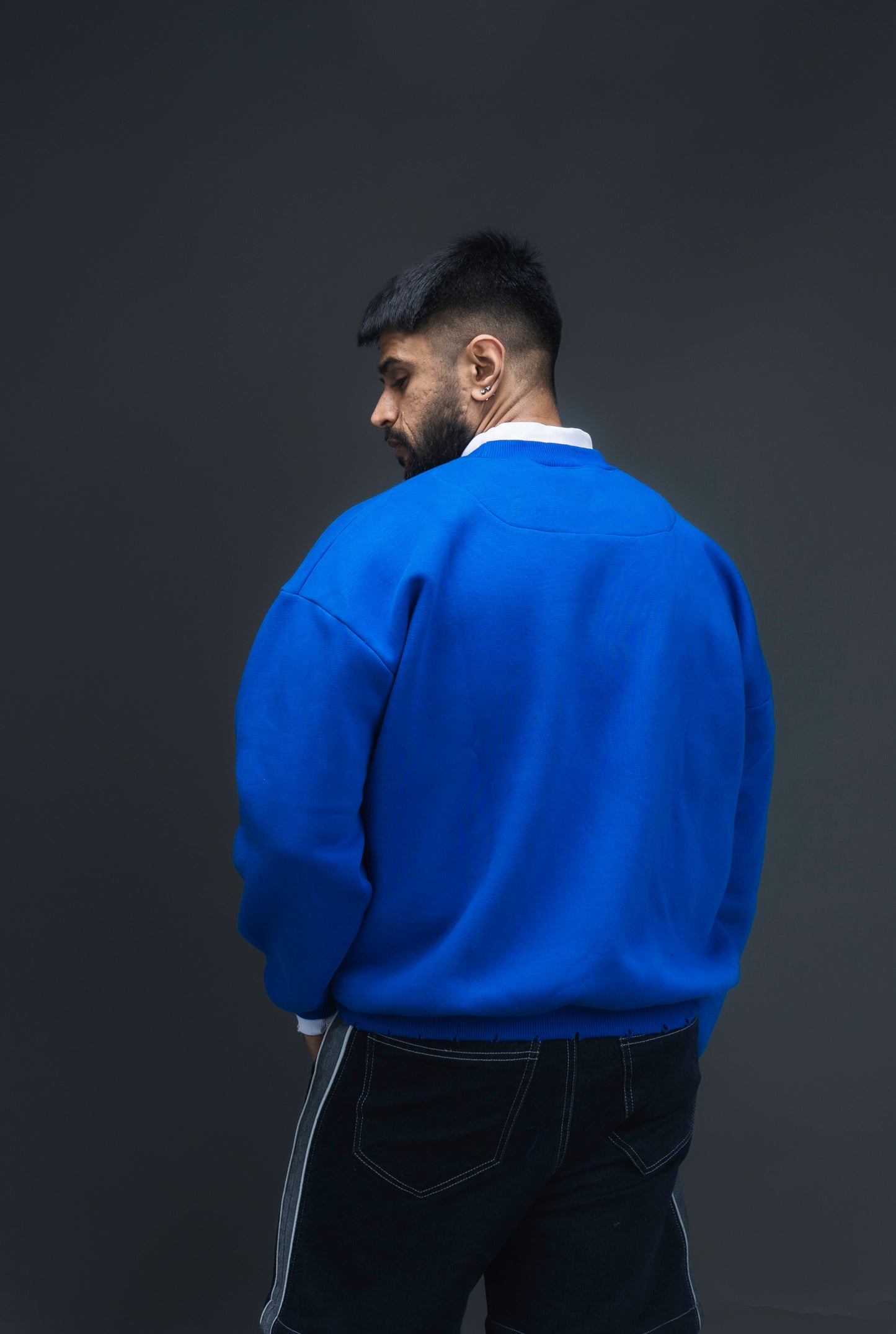 Man wearing ORE OFE's blue contrast sweatshirt with the logo on the centre of the chest standing against a grey background