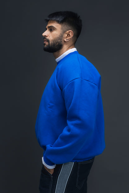 Man wearing ORE OFE's blue contrast sweatshirt with the logo on the centre of the chest standing against a grey background