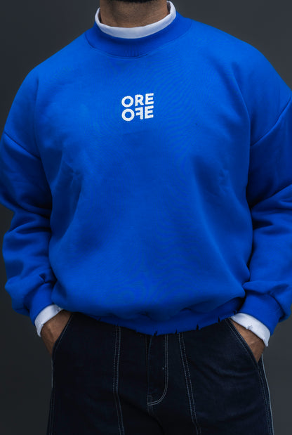 Man wearing ORE OFE's blue contrast sweatshirt with the logo on the centre of the chest standing against a grey background