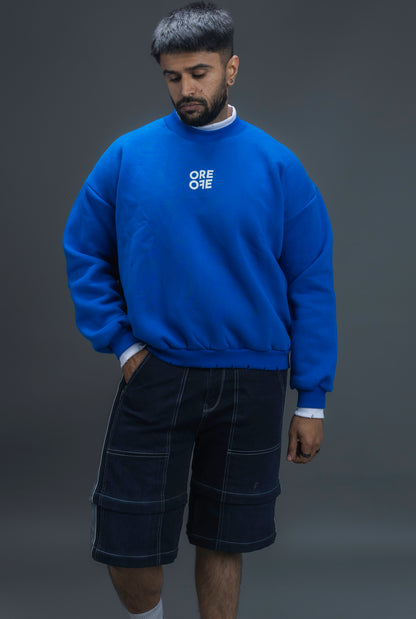 Man wearing ORE OFE's blue contrast sweatshirt with the logo on the centre of the chest standing against a grey background