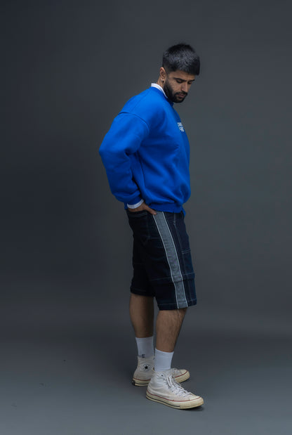 Man wearing ORE OFE's blue contrast sweatshirt with the logo on the centre of the chest standing against a grey background