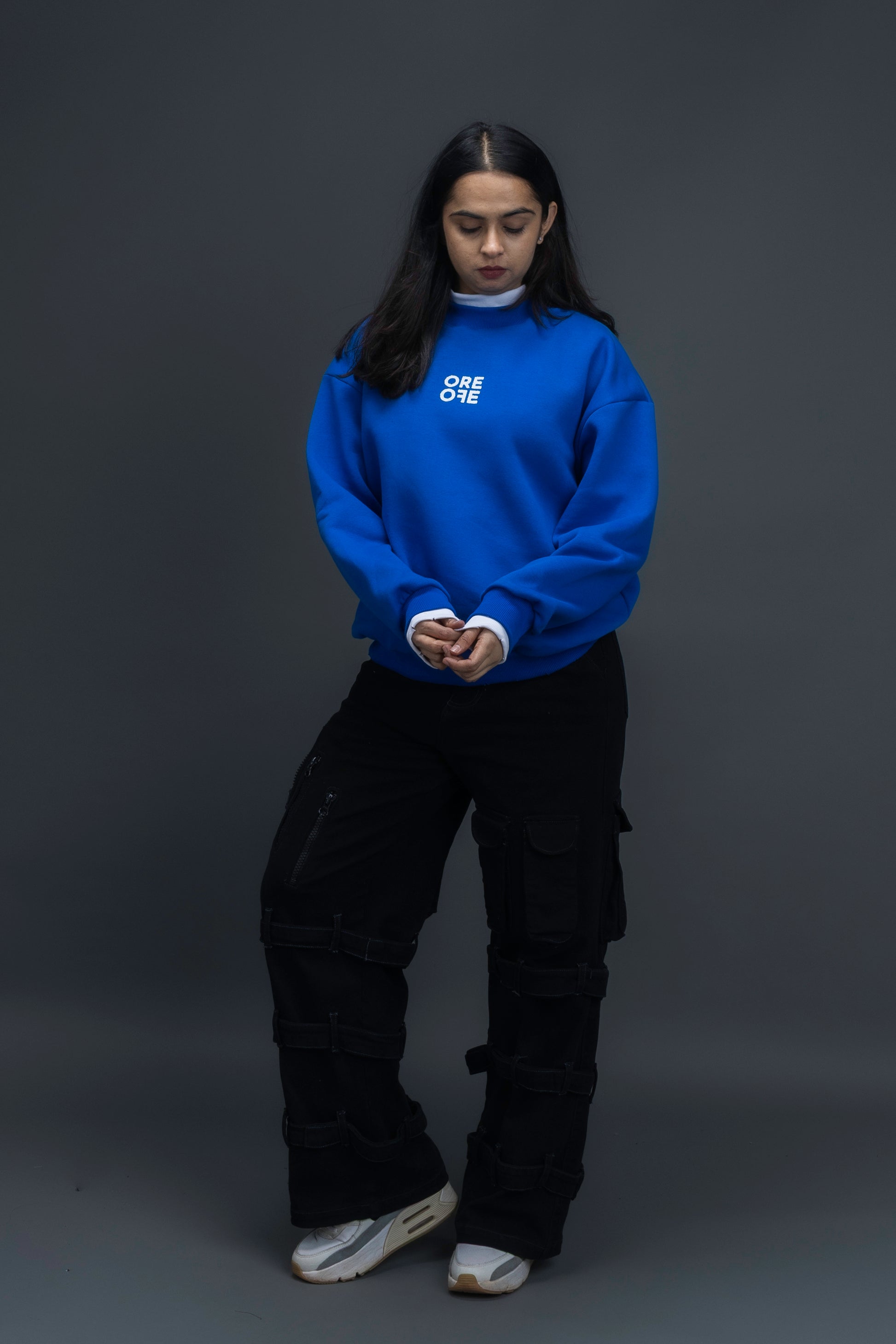 Person wearing a blue sweatshirt with ORE OFE logo on the centre of the chest standing against a grey background