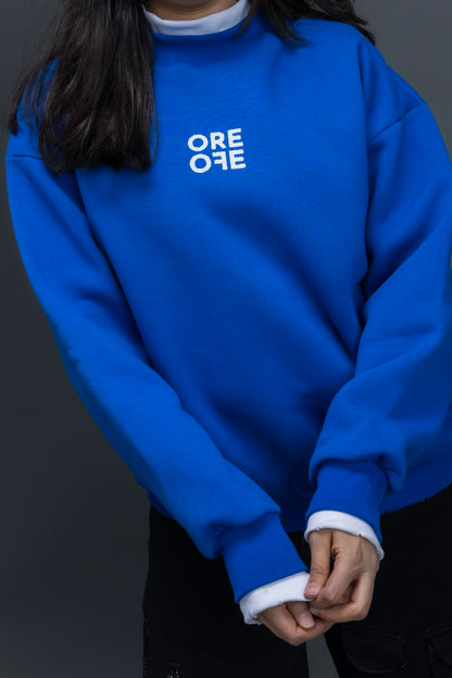 Person wearing a blue sweatshirt with ORE OFE logo on the centre of the chest standing against a grey background