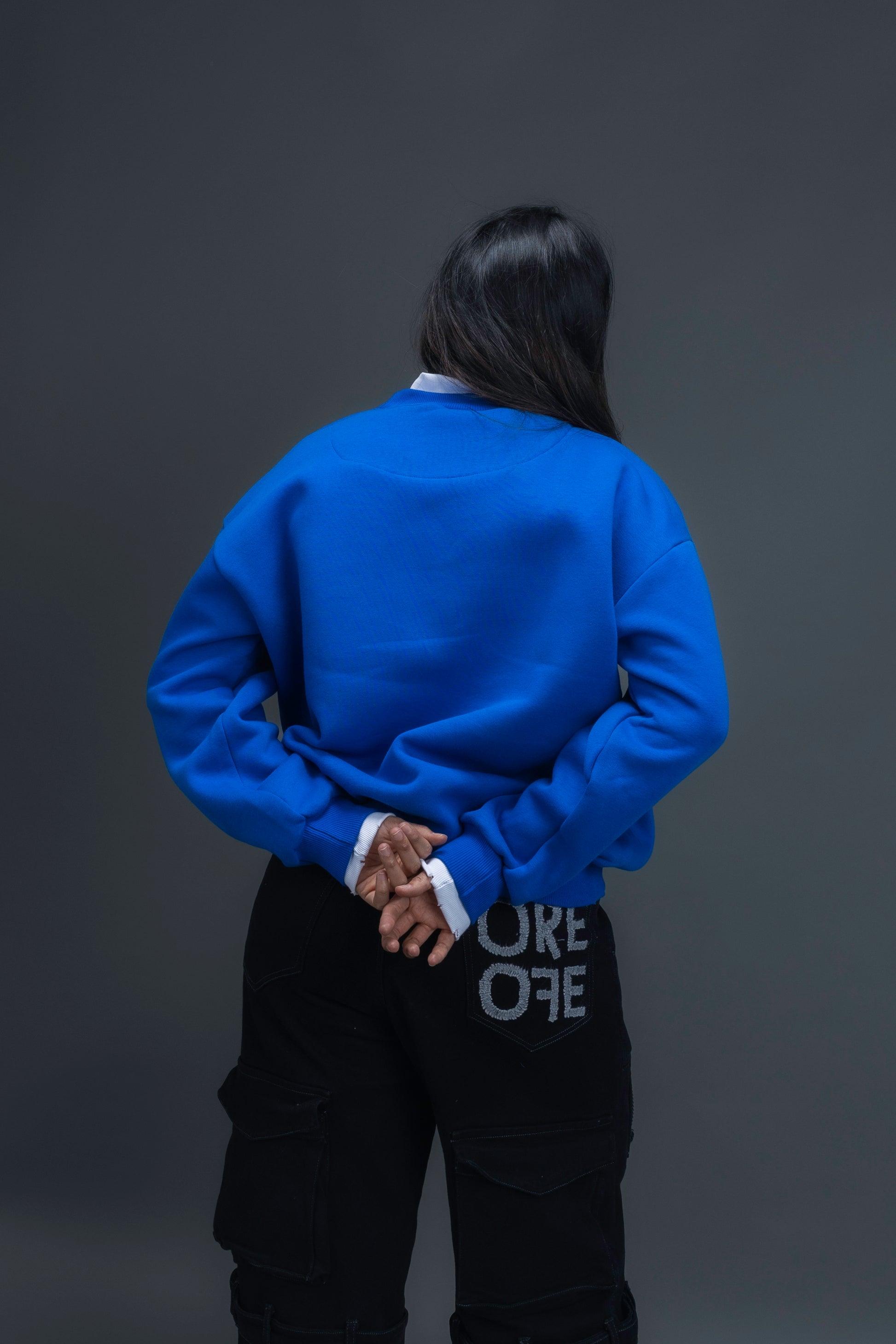 Person wearing a blue sweatshirt with ORE OFE logo on the centre of the chest standing against a grey background