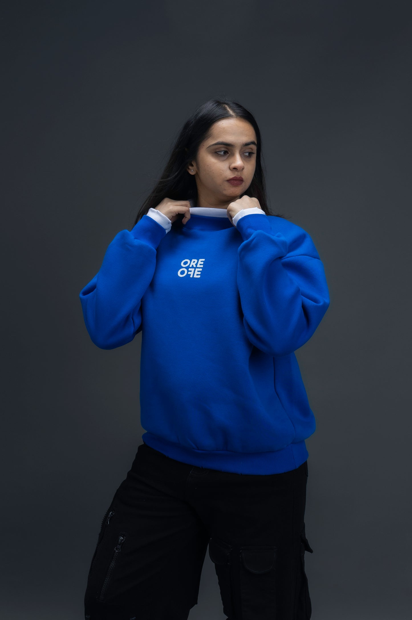 Person wearing a blue sweatshirt with ORE OFE logo on the centre of the chest standing against a grey background