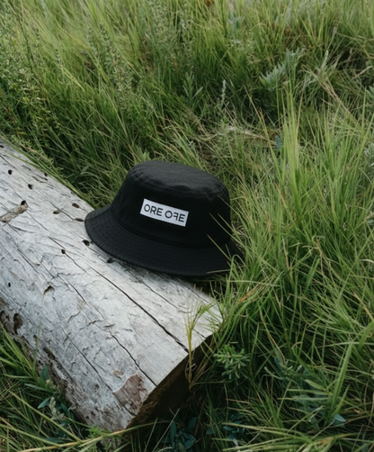Black bucket hat with a brand logo on a log in a grassy area