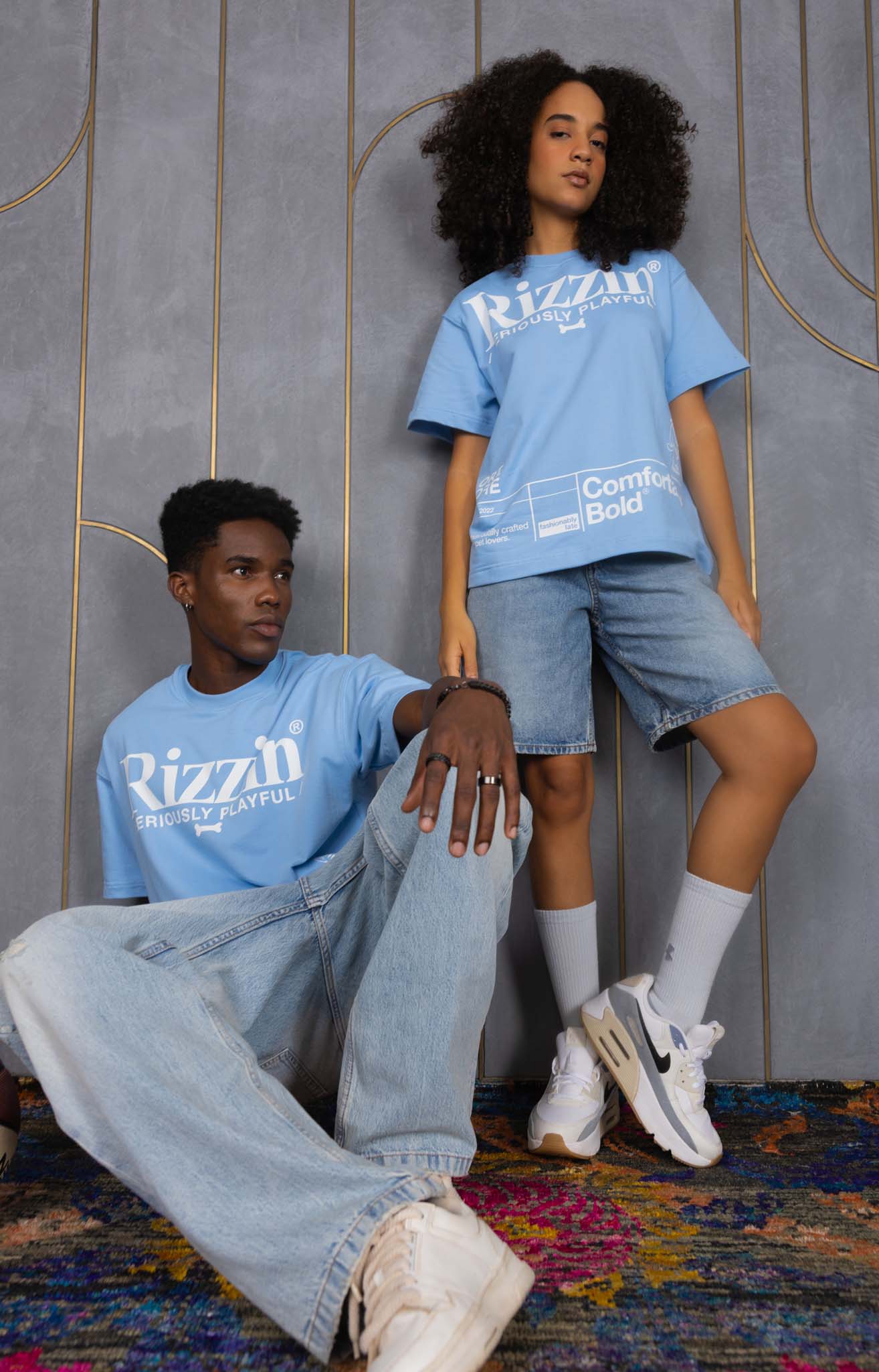 Two people wearing blue 'Rizzin' t-shirts in a room with decorative elements.