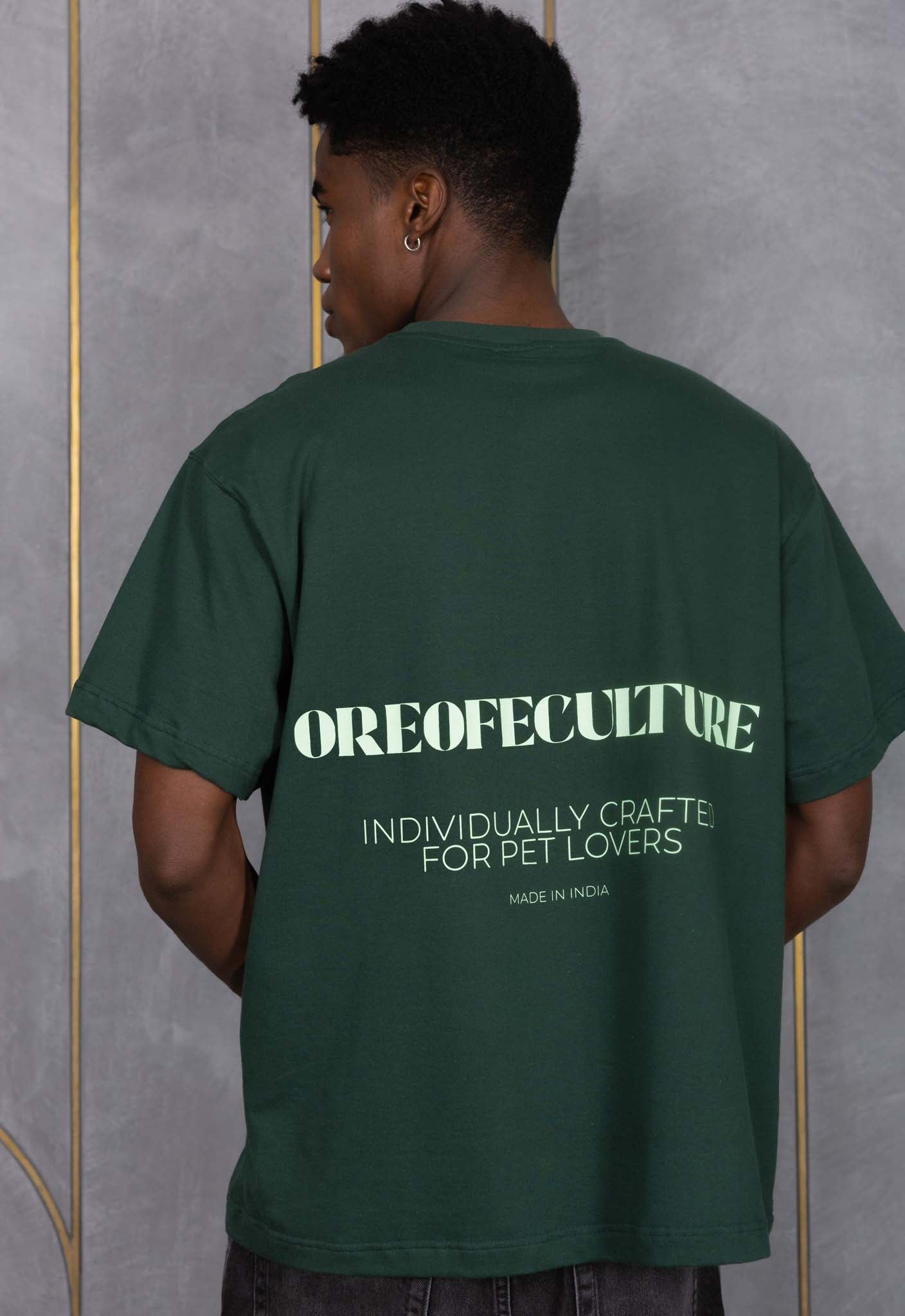 Person wearing a green t-shirt with text on the back against a gray wall.