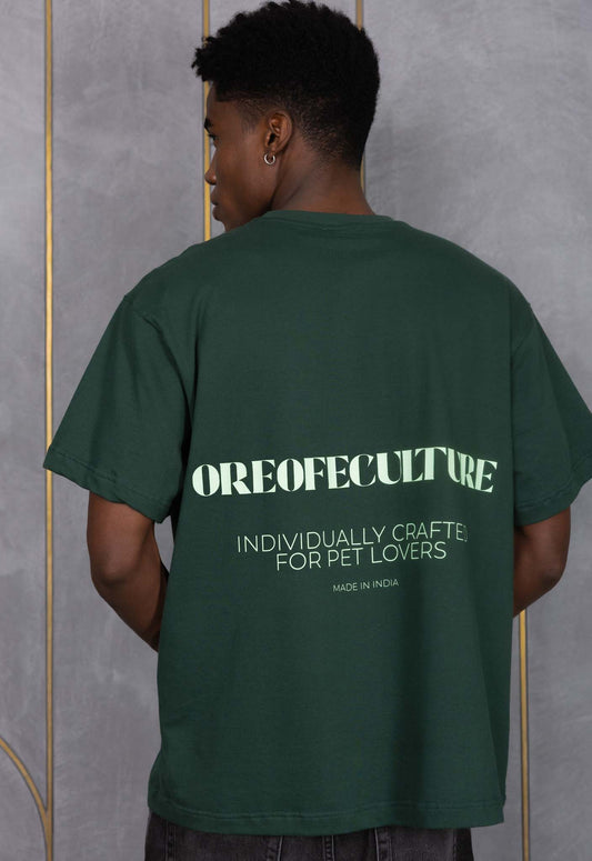 Person wearing a green t-shirt with text on the back against a gray wall.