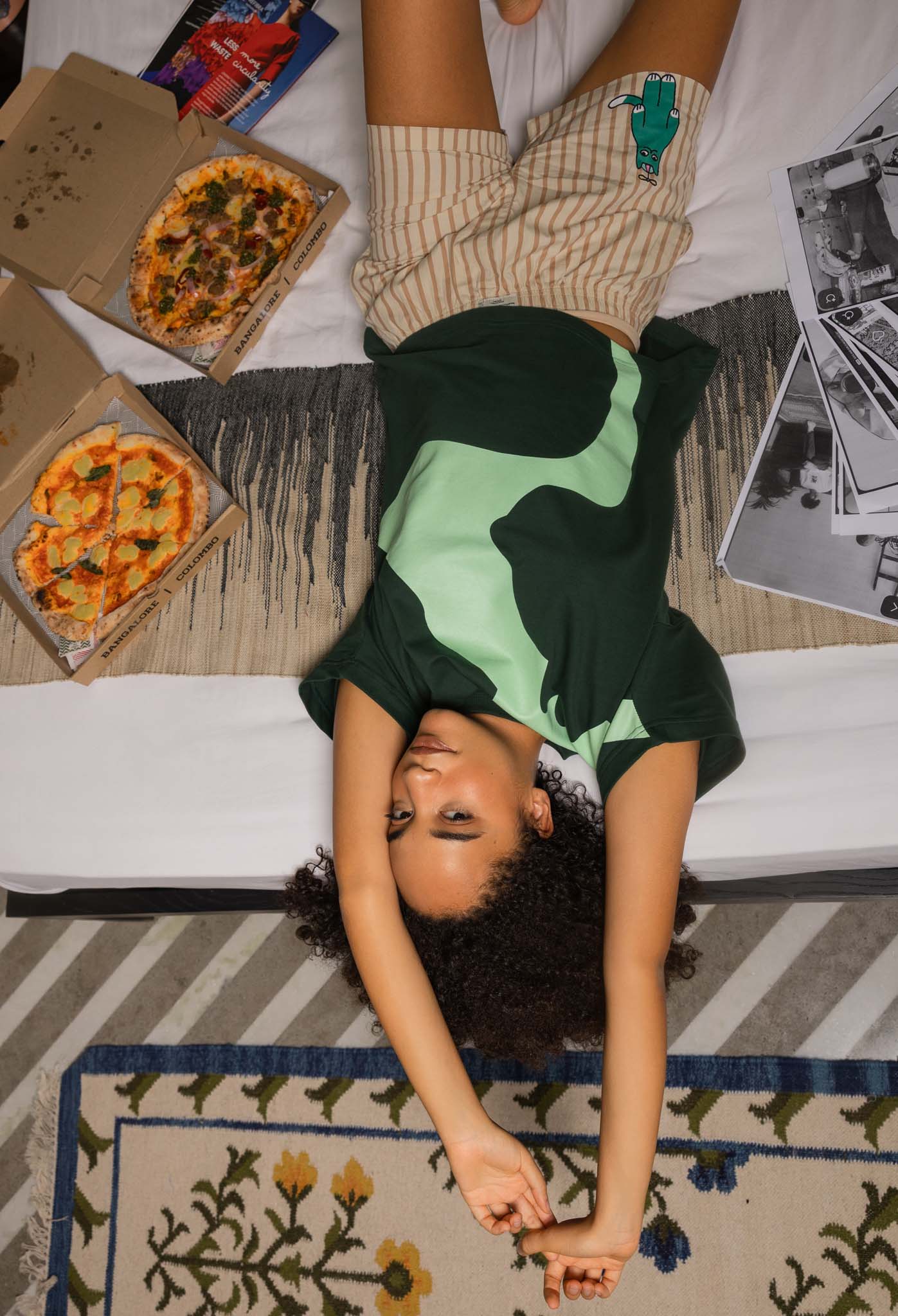 Person lying on a rug with pizza boxes and photos around
