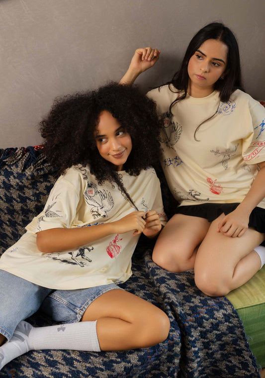 Two women sitting on a patterned couch wearing matching white t-shirts with colorful designs.