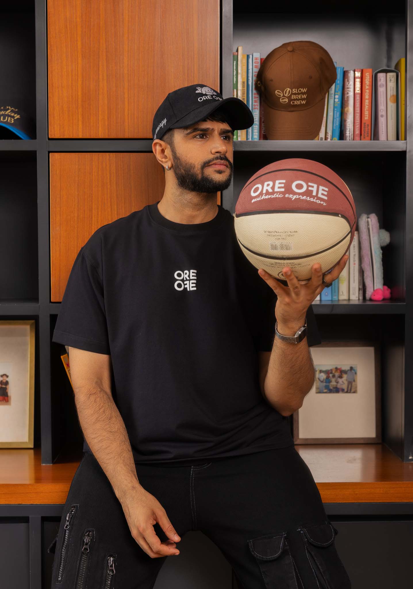 Man holding a basketball with 'ORE OFE' branding in front of a bookshelf.