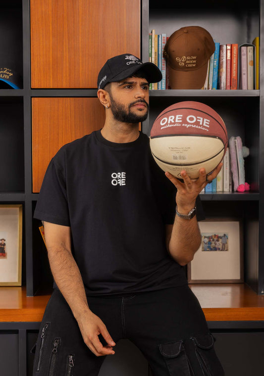 Man holding a basketball with 'ORE OFE' branding in front of a bookshelf.