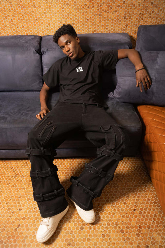Person wearing a black outfit sitting on a couch with a patterned wall and floor.