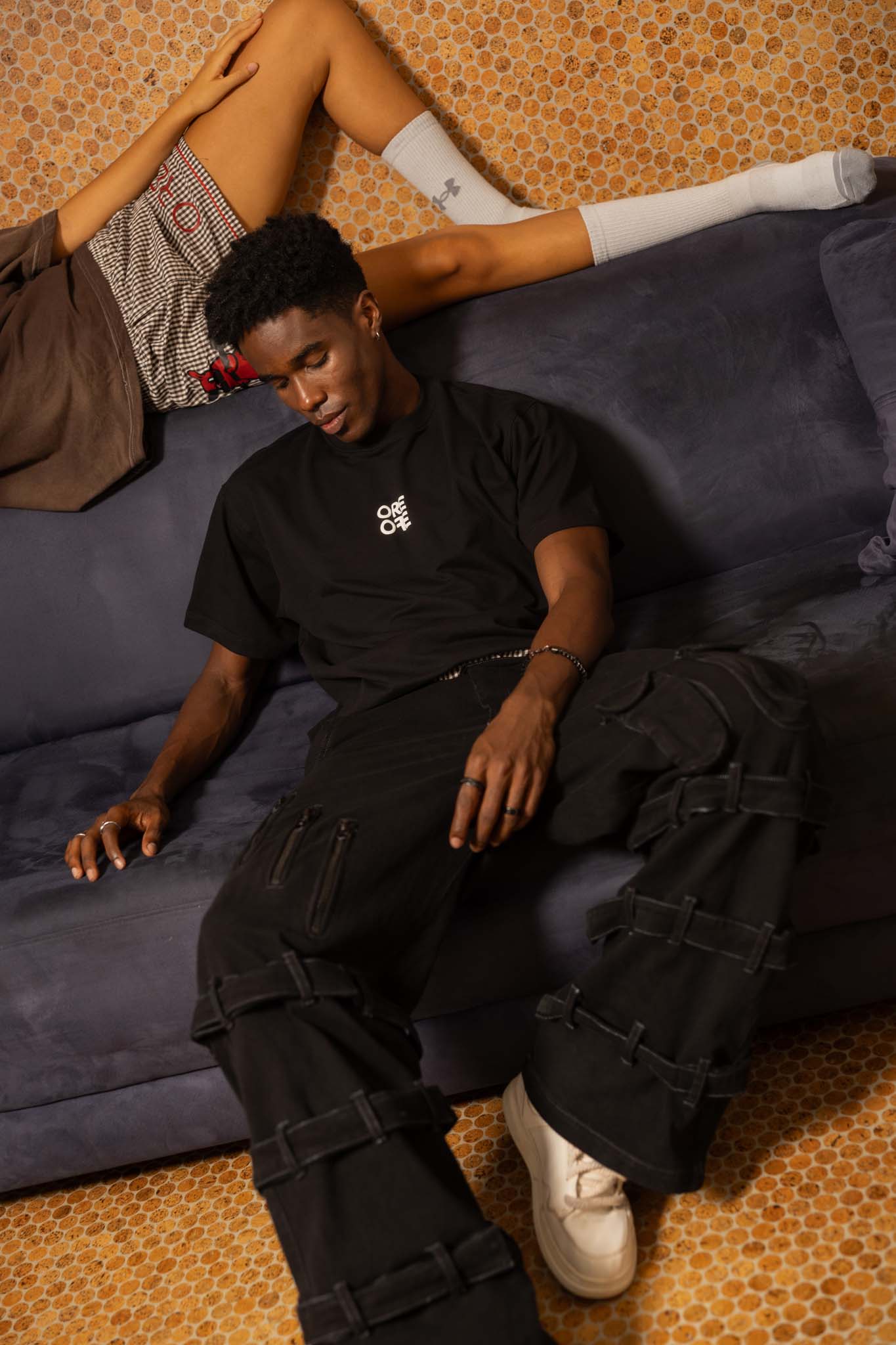 Person wearing a black t-shirt and cargo pants sitting on a blue couch.