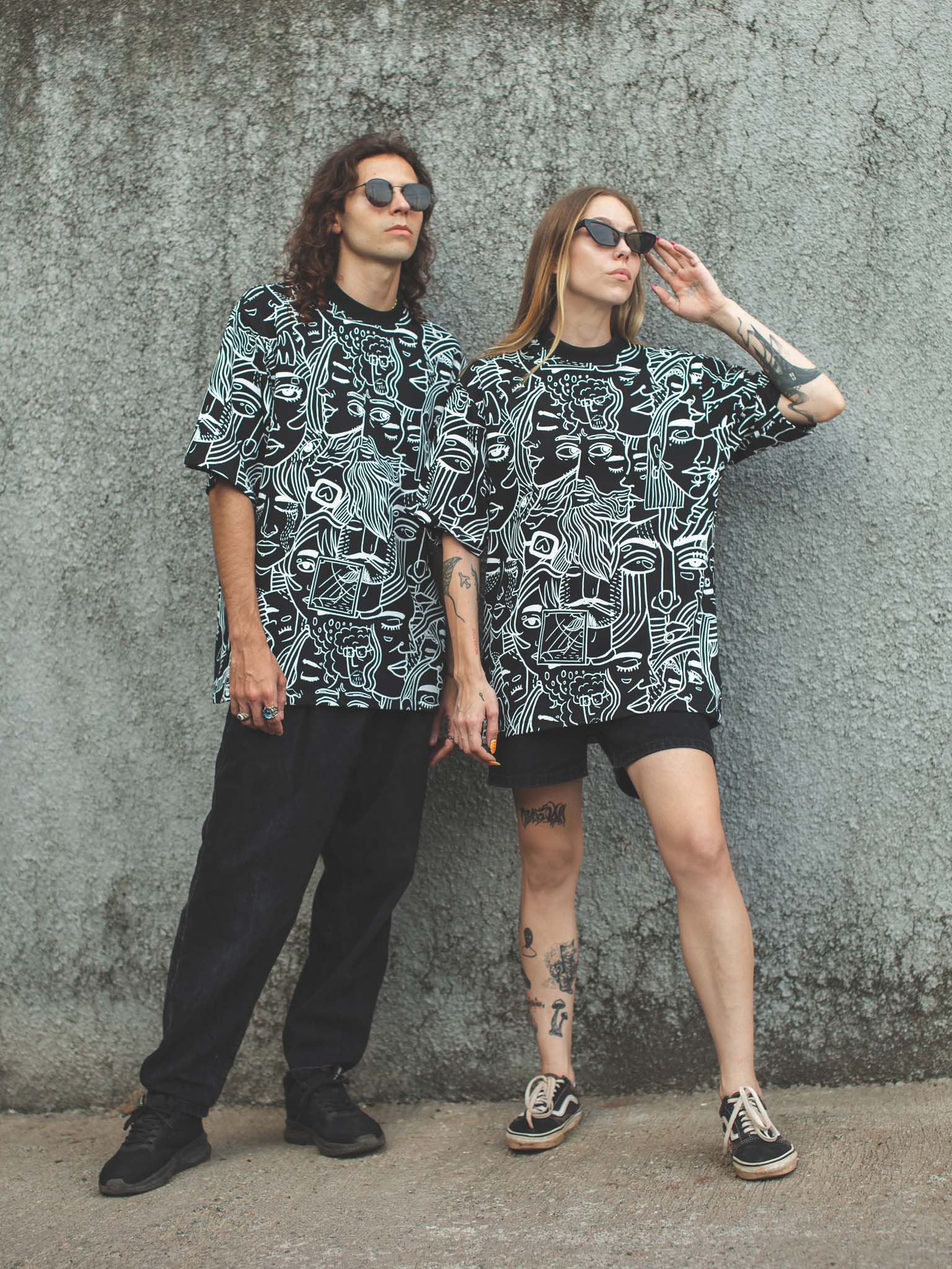 Two people wearing matching black and white patterned shirts against a gray wall.
