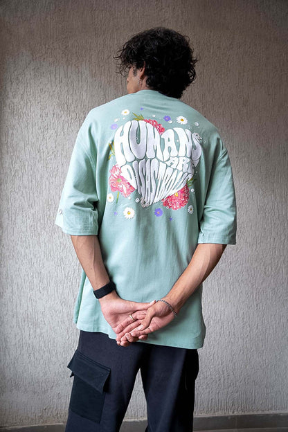 Person wearing a light green shirt with a colorful design on the back against a plain wall.