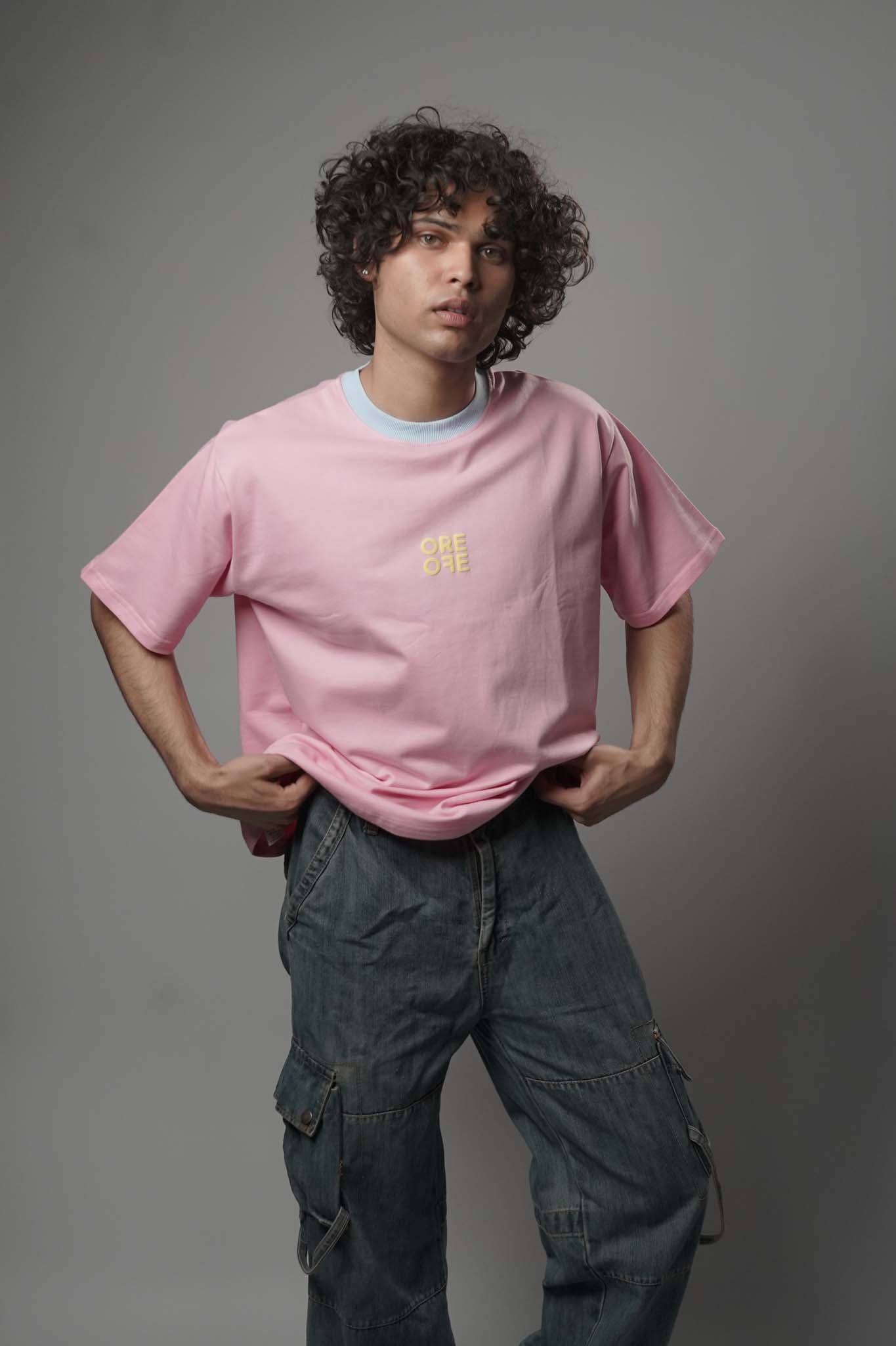 Person wearing a pink t-shirt with a logo and dark pants against a gray background