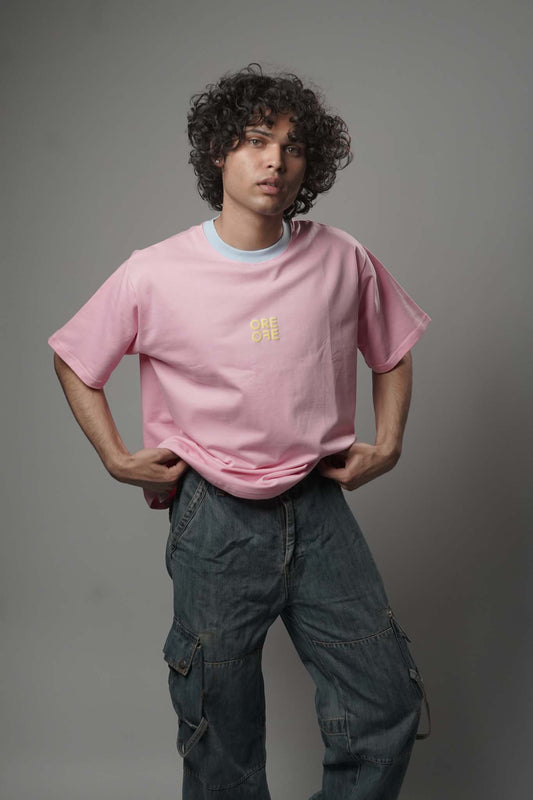 Person wearing a pink t-shirt with a logo and dark pants against a gray background