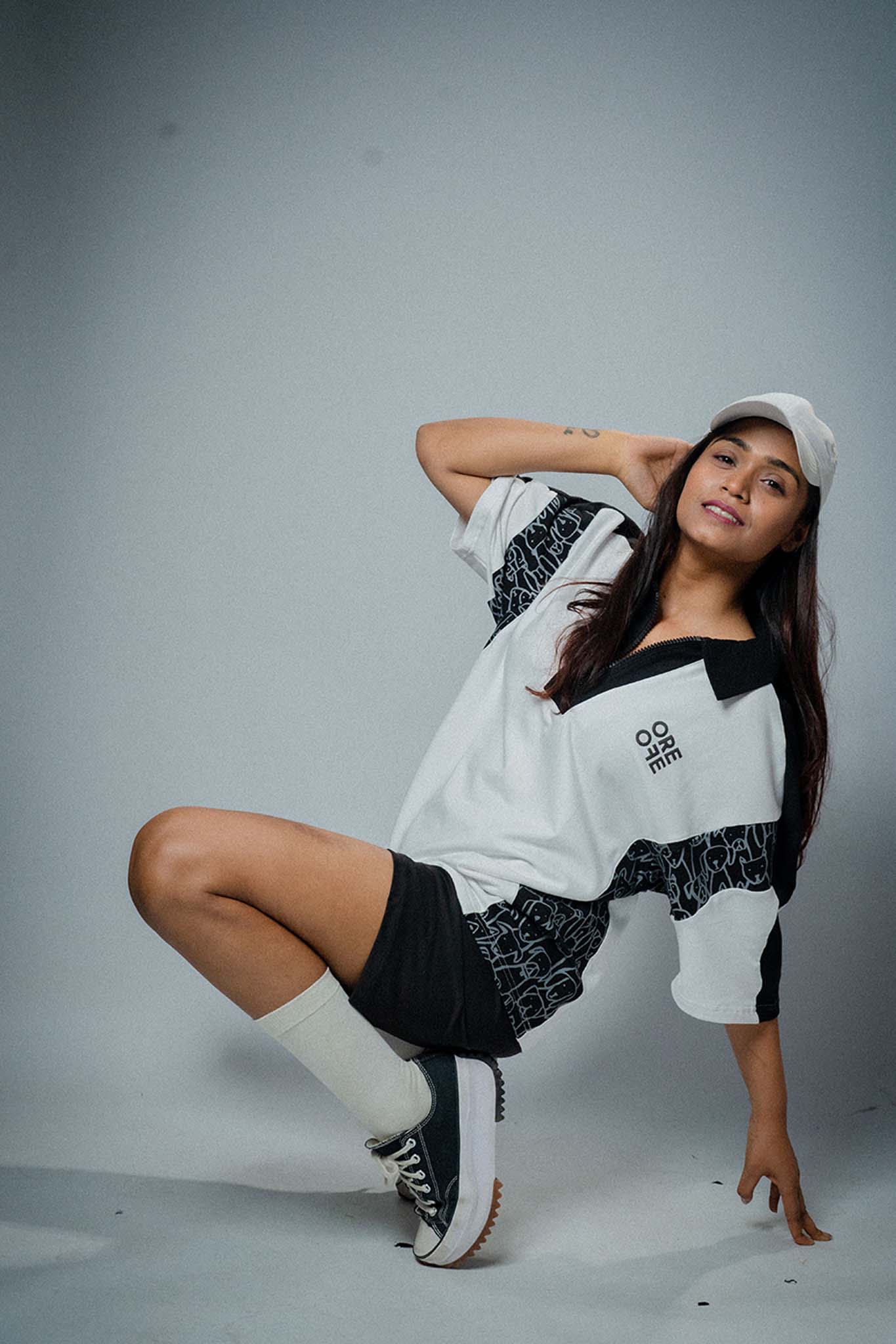 Woman posing in a stylish outfit with a white and black top and shorts on a gray background