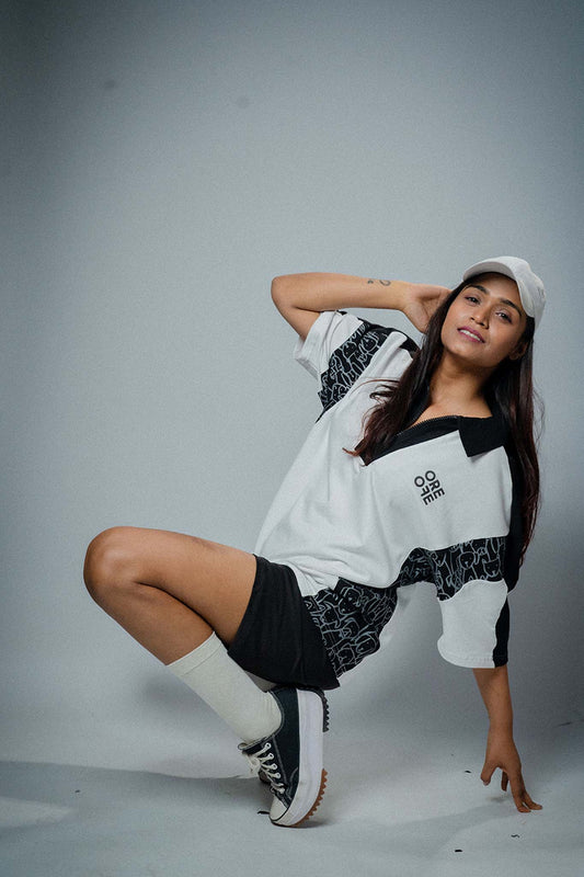 Woman posing in a stylish outfit with a white and black top and shorts on a gray background