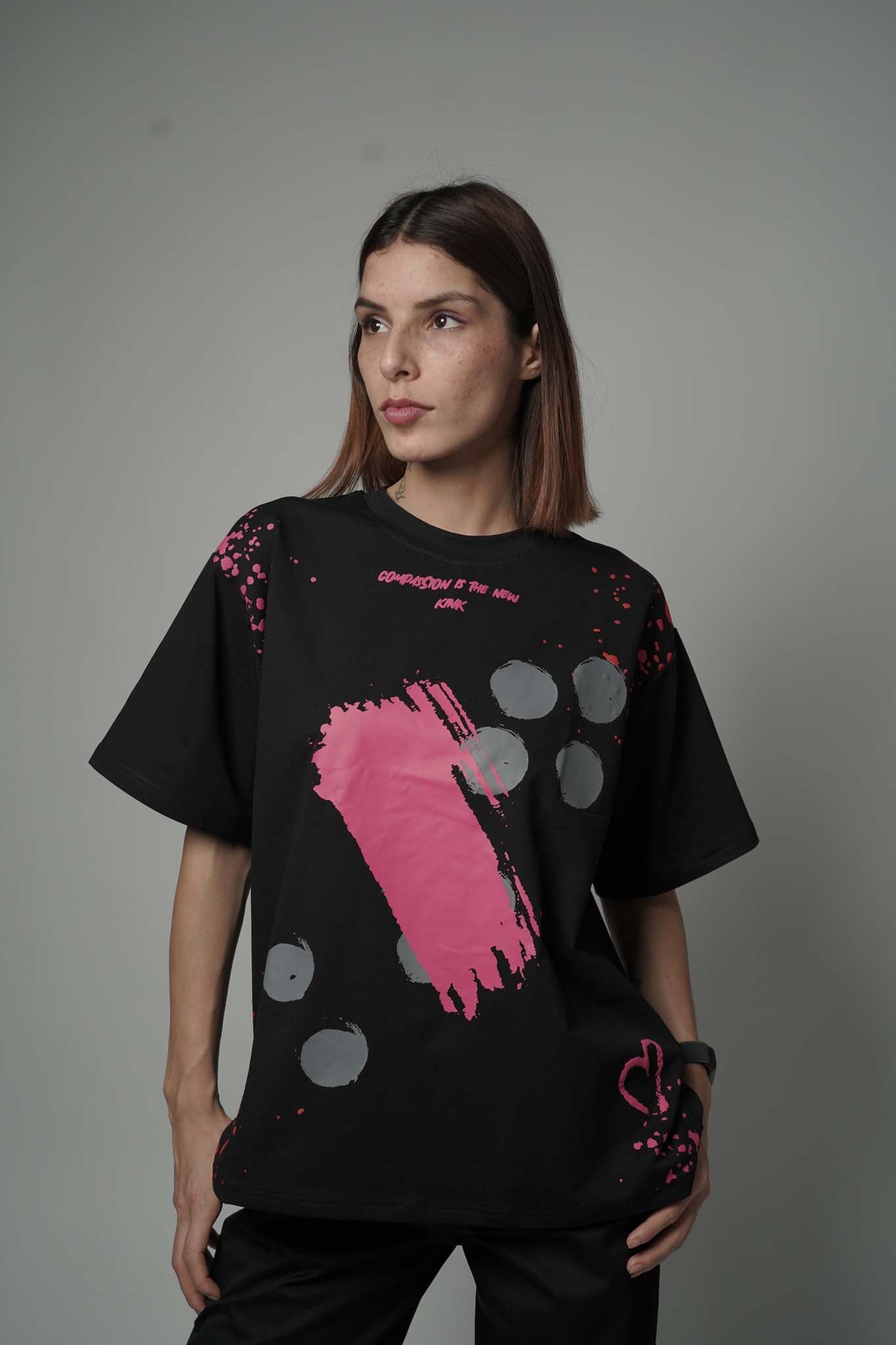 Person wearing a black t-shirt with pink and gray abstract design on a plain background