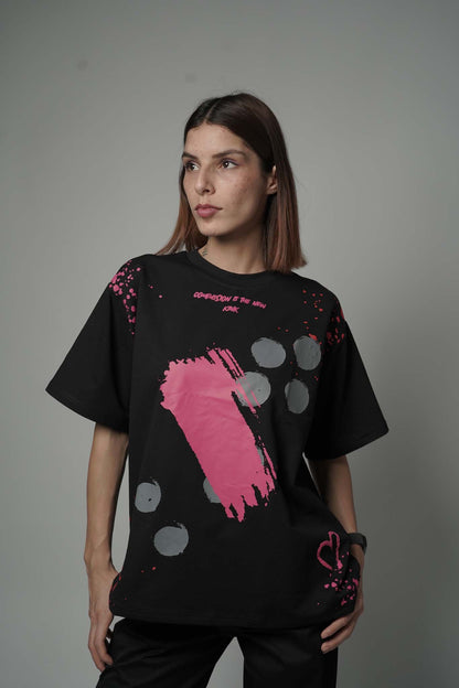 Person wearing a black t-shirt with pink and gray abstract design on a plain background