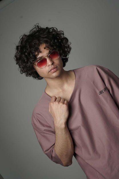 Person wearing a mauve shirt and red sunglasses against a plain background