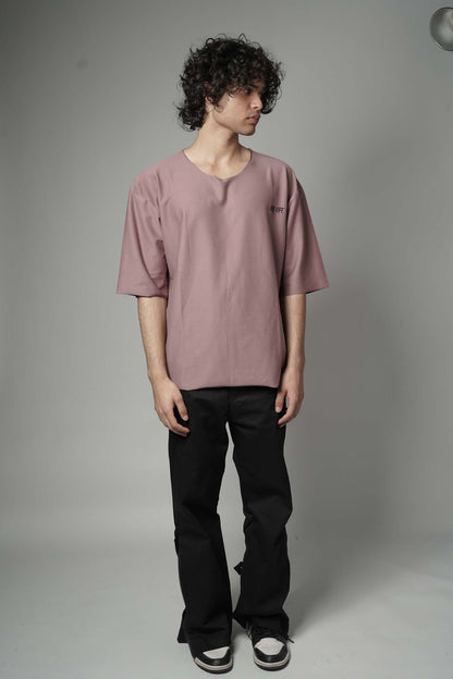 Person wearing a mauve t-shirt and black pants against a plain background