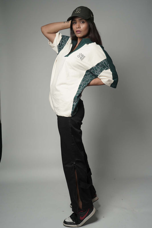 Person wearing a beige and green polo t-shirt with a logo, black pants, and a black cap on a gray background