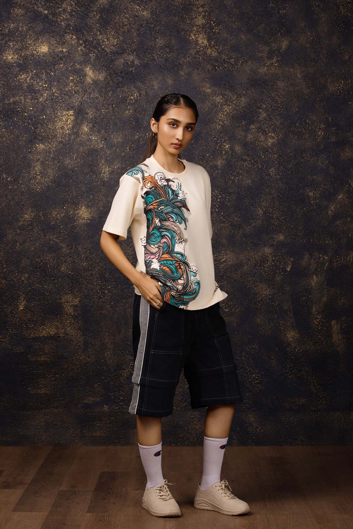 Person wearing a beige t-shirt with colorful graphics and black shorts against a textured dark background