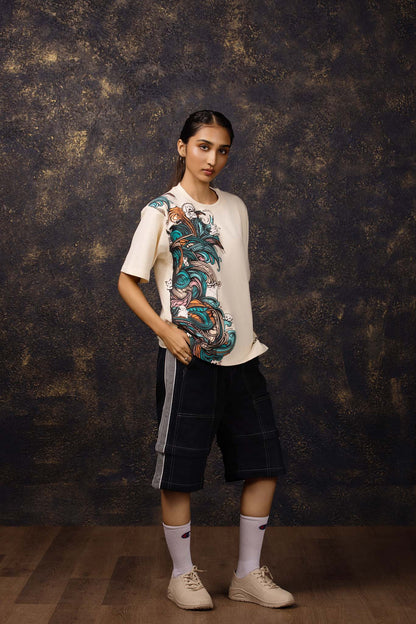 Person wearing a beige t-shirt with colorful graphics and black shorts against a textured dark background