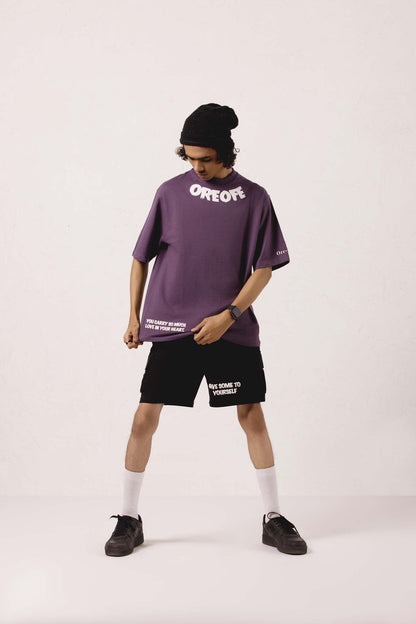 Person wearing a purple oversized t-shirt and black shorts with visible branding on a white background