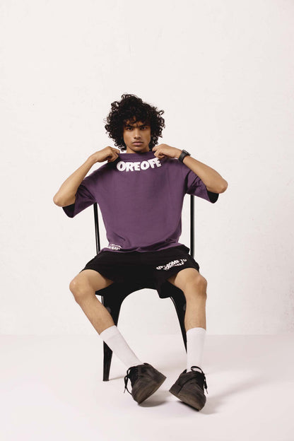 Person wearing a purple shirt with text, sitting on a chair against a white background