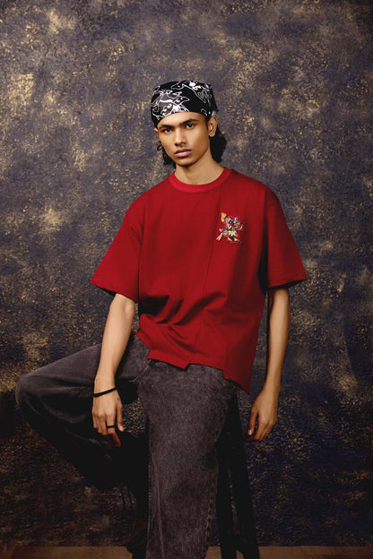 Person wearing a red shirt with a graphic design and dark pants against a textured brown background