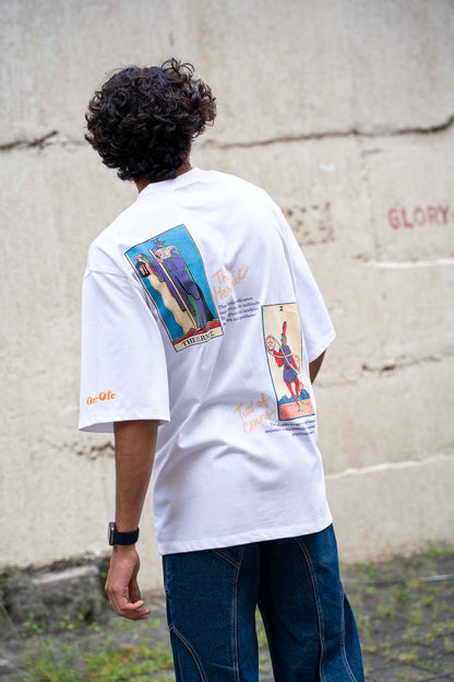 Person wearing a white t-shirt with graphic designs on the back, standing against a concrete wall.