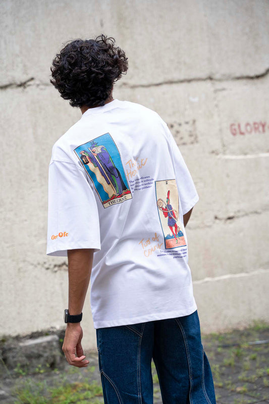 Person wearing a white t-shirt with graphic designs on the back, standing against a concrete wall.