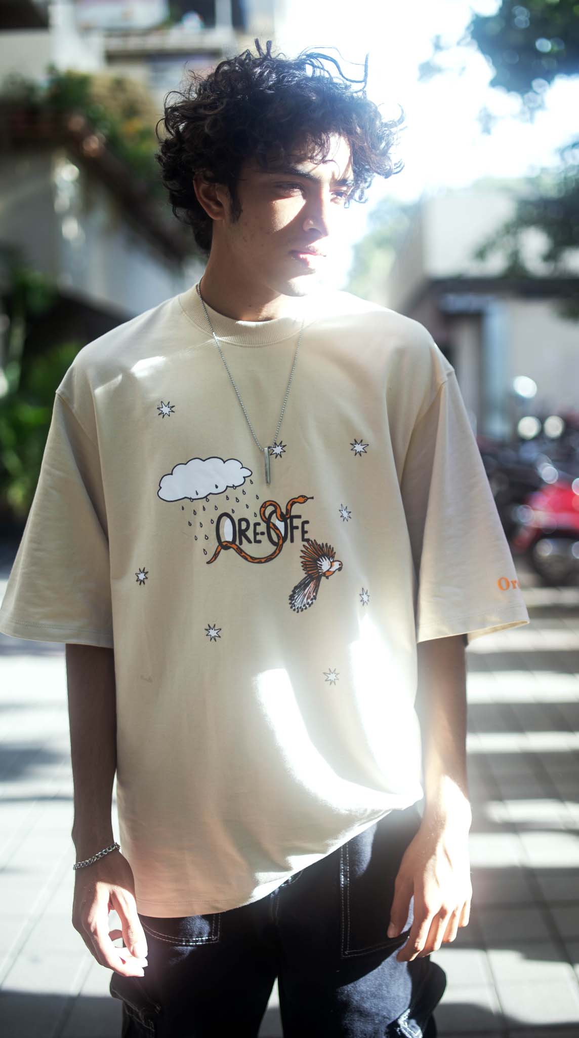 Person wearing a beige t-shirt with graphics and text outdoors