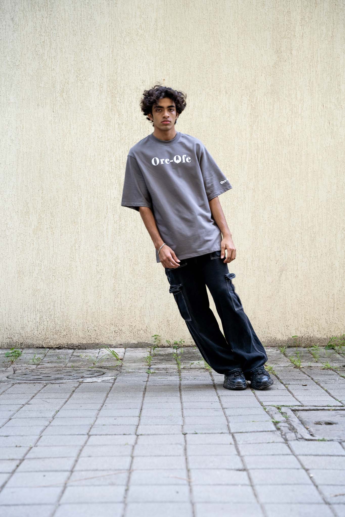 Person wearing a gray t-shirt with text, standing against a plain wall.